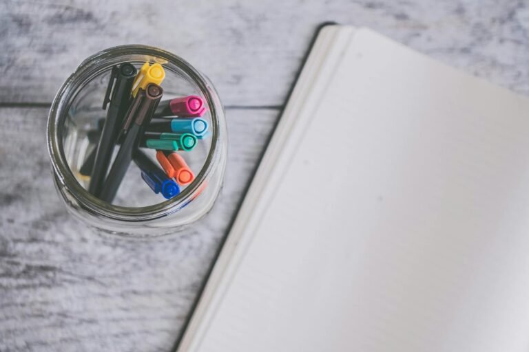 clear glass jar filled of coloring pens beside of white sketch pad